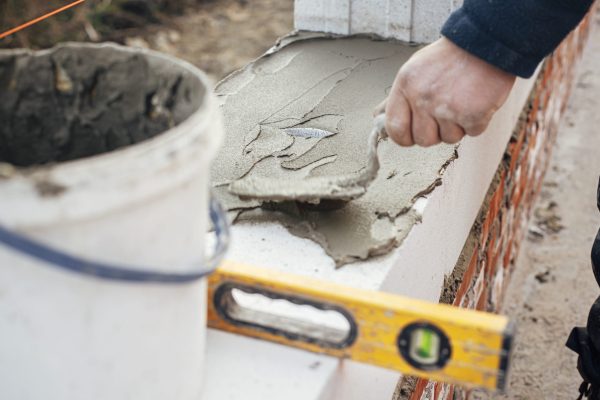 Worker laying autoclaved aerated concrete blocks, working with adhesive and trowel. Builder installing masonry white blocks close up. Process of house building at construction site